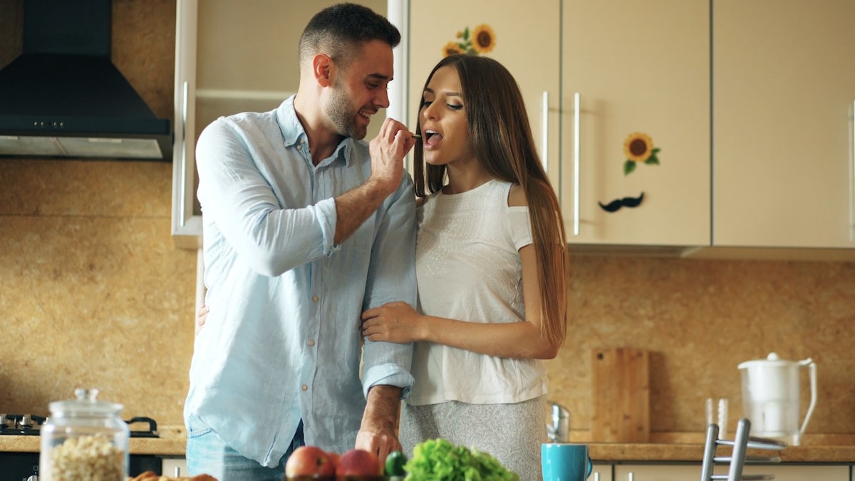 Happy young couple in the kitchen. Handsome man meet and feed his girlfriend early morning at home